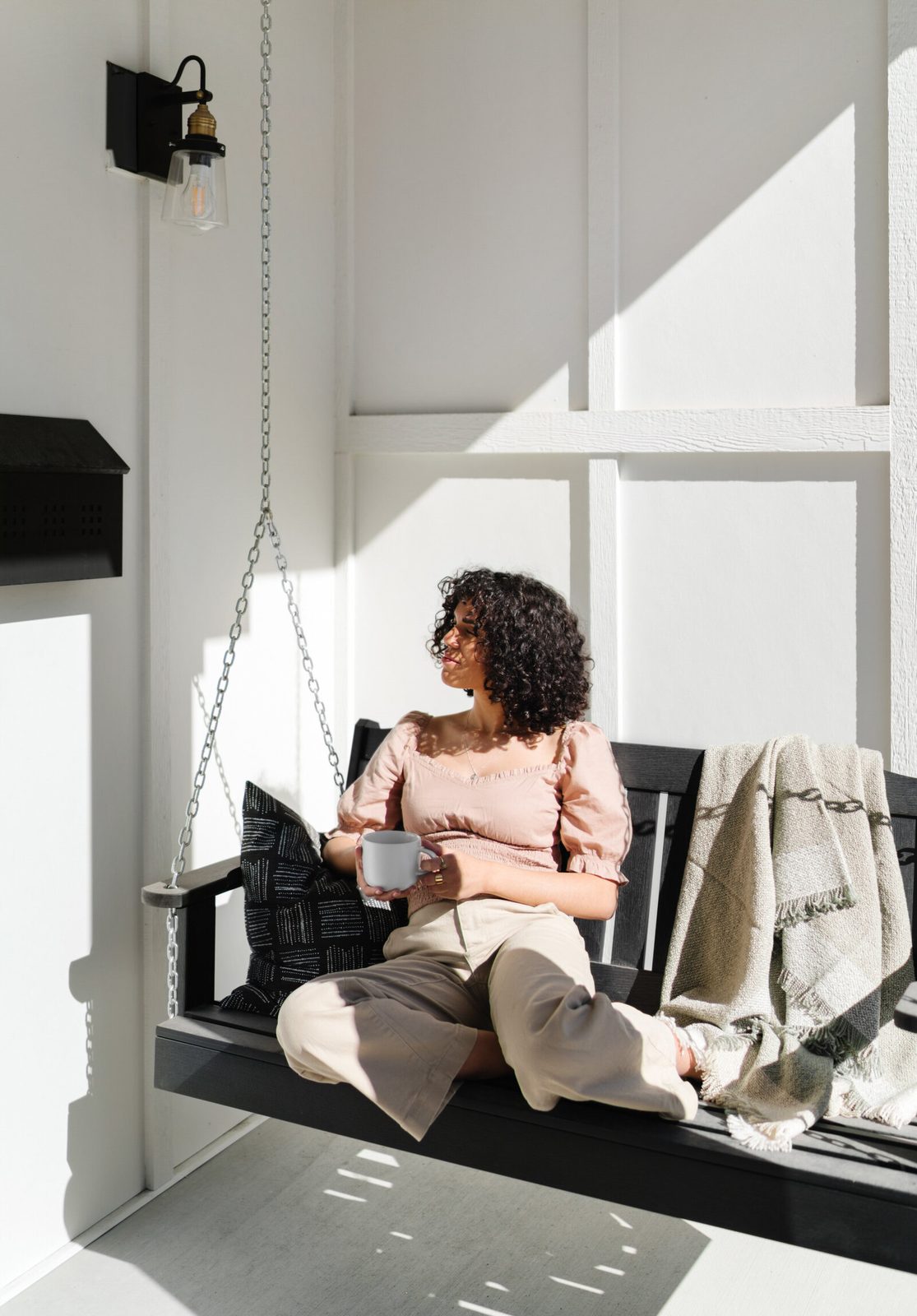 Person seated on a porch swing beside a light-colored house