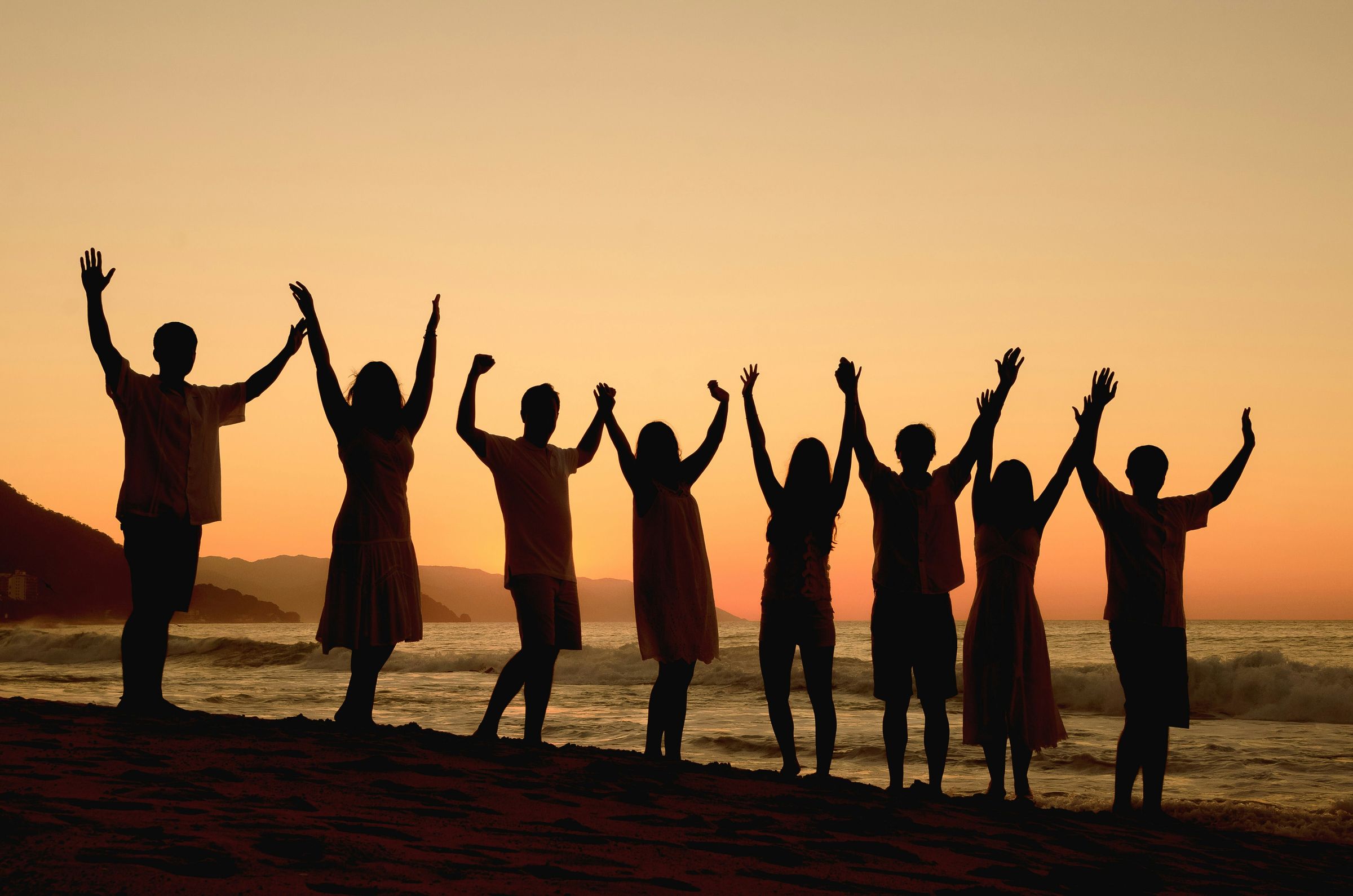 Friends raising their arms on a beach at sunset